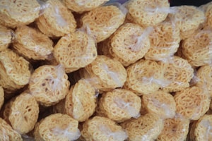 A large number of round, tightly packed bundles of dried noodles are wrapped in plastic. The noodles have a light yellow color and are arranged closely together.