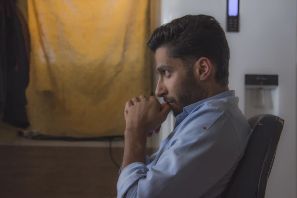Close-up of a thoughtful man with a calm expression, sitting in a serene space with soft blue and gold accents.