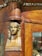 A carved wooden structure features a small, intricate bust of an Egyptian-style figure integrated into the corner of a wooden frame. The wood is polished, showcasing rich brown tones and detailed craftsmanship in both the sculpture and the surrounding woodwork.
