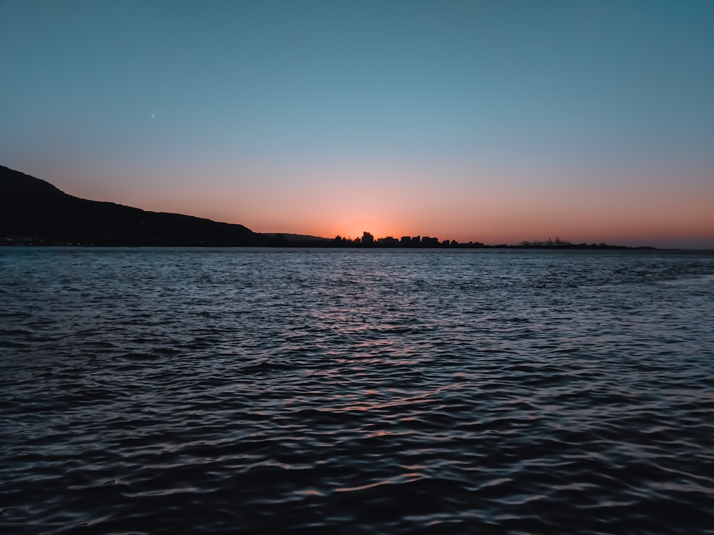 Silueta de la montaña cerca del cuerpo de agua durante la puesta del sol