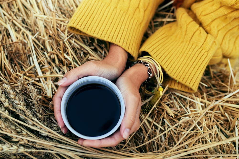 Persona che tiene la tazza di ceramica bianca con liquido nero