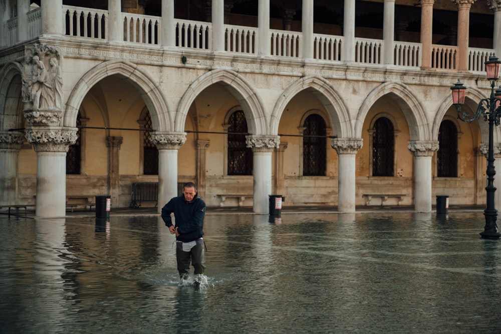 person in black jacket and black pants standing on water near beige concrete building during daytime