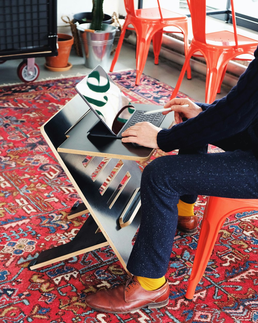 person in black pants sitting on orange plastic chair reading magazine