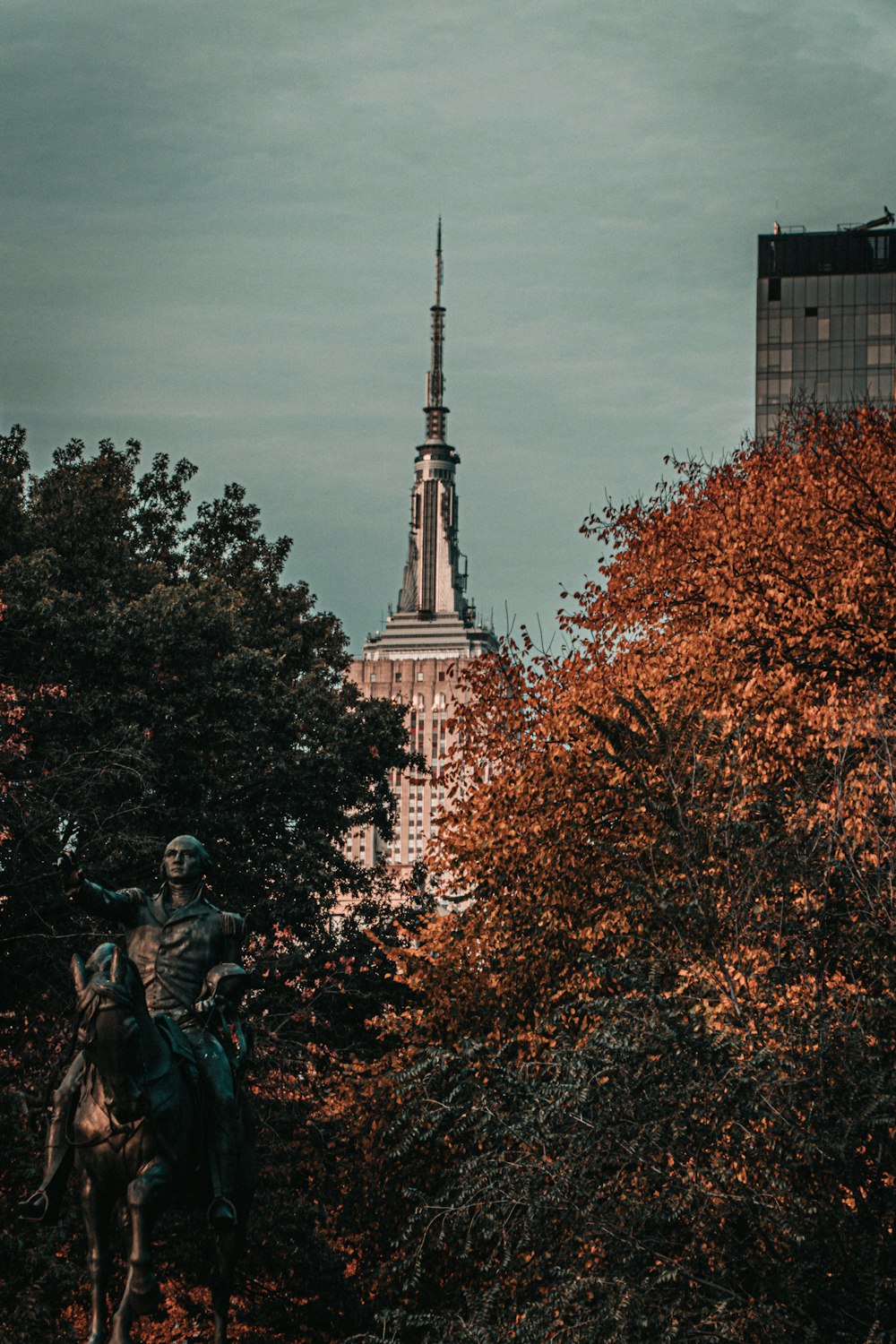 Statue d’homme et de femme près d’arbres bruns sous des nuages blancs pendant la journée