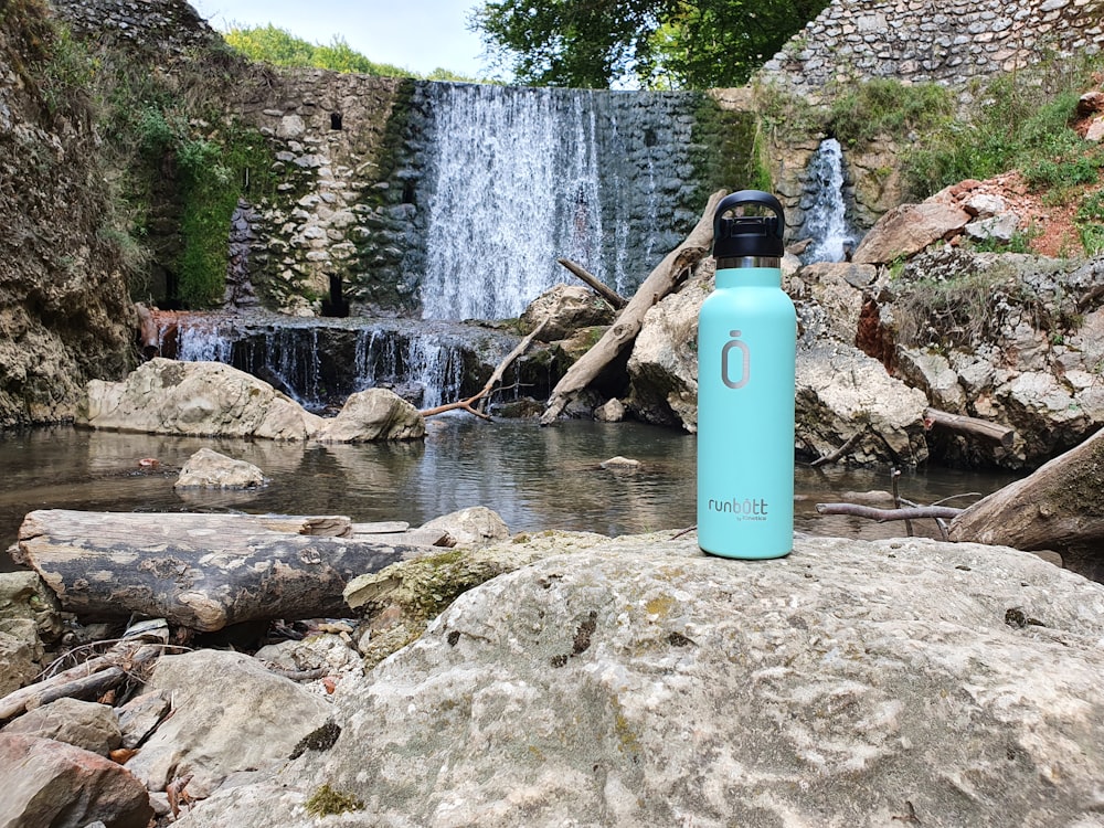 blue and black sports bottle on gray rock near body of water during daytime