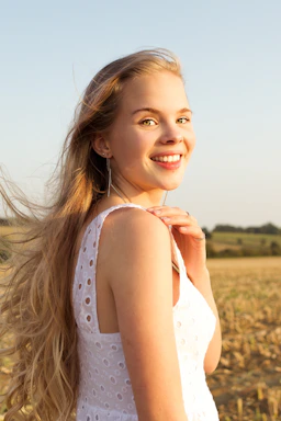 A carefree young woman in a flowing boho dress standing in a sunlit meadow with wildflowers.