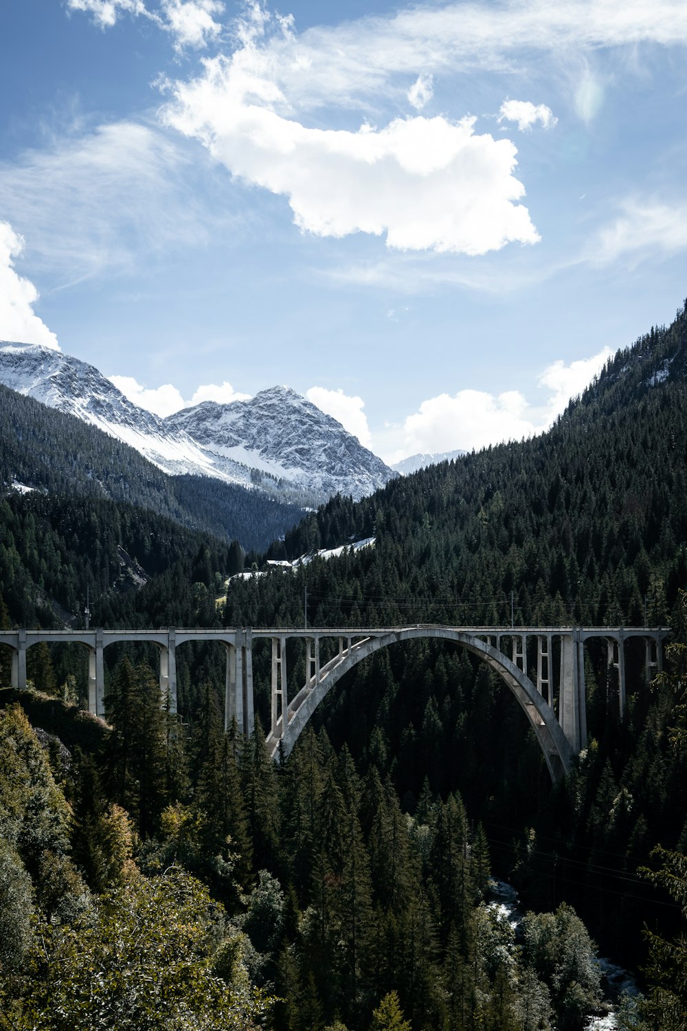 white bridge over river near green trees and mountains during daytime