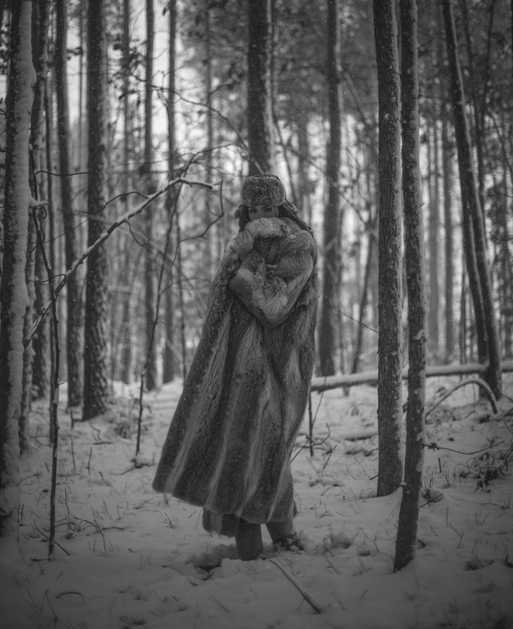 grayscale photo of person in winter coat standing in forest