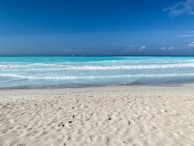 A serene beach with turquoise waves gently rolling onto white sand under a bright blue sky.