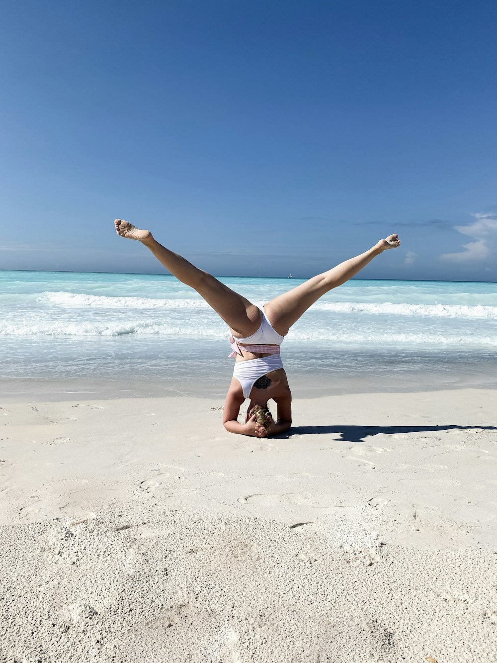 Frau in weißem Tanktop und weißen Shorts springt tagsüber am Strand