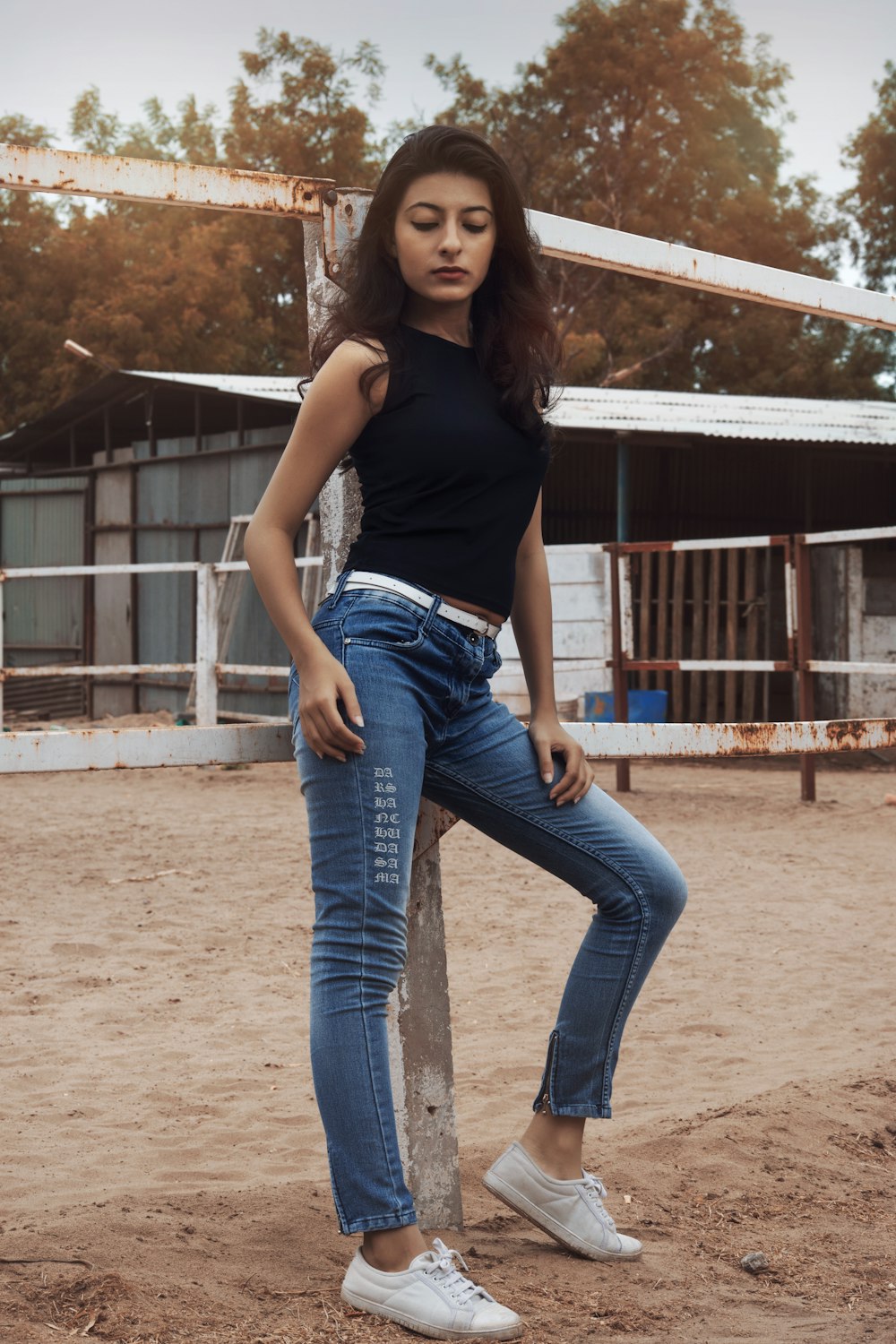 woman in black tank top and blue denim jeans standing on brown sand during daytime