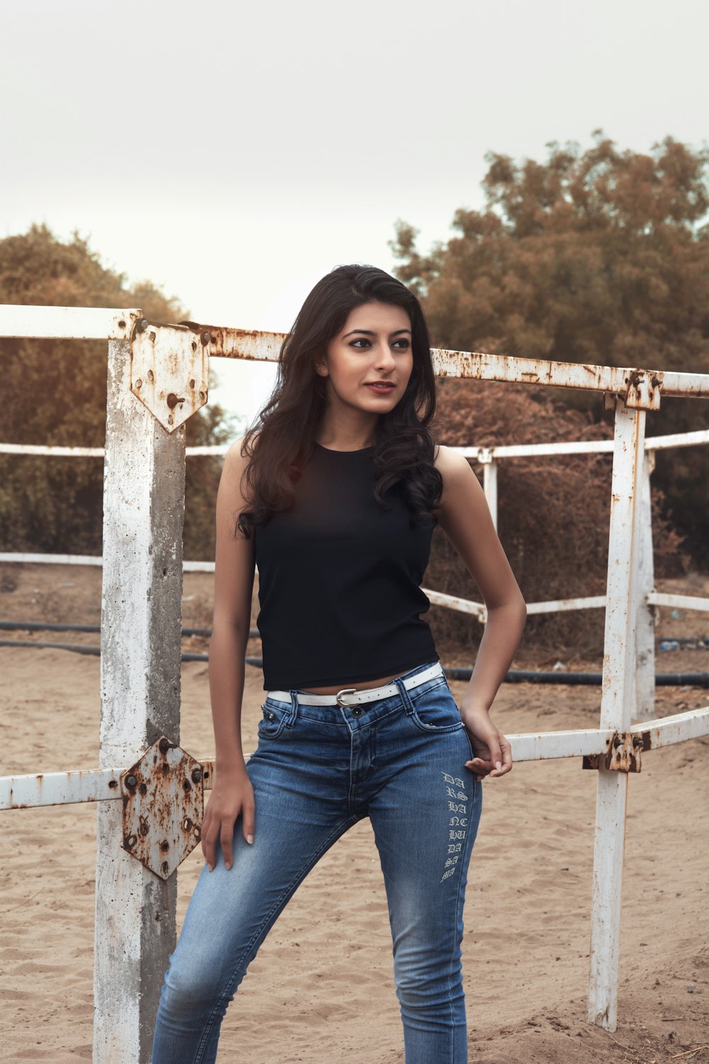 woman in black tank top and blue denim jeans standing beside brown wooden fence during daytime