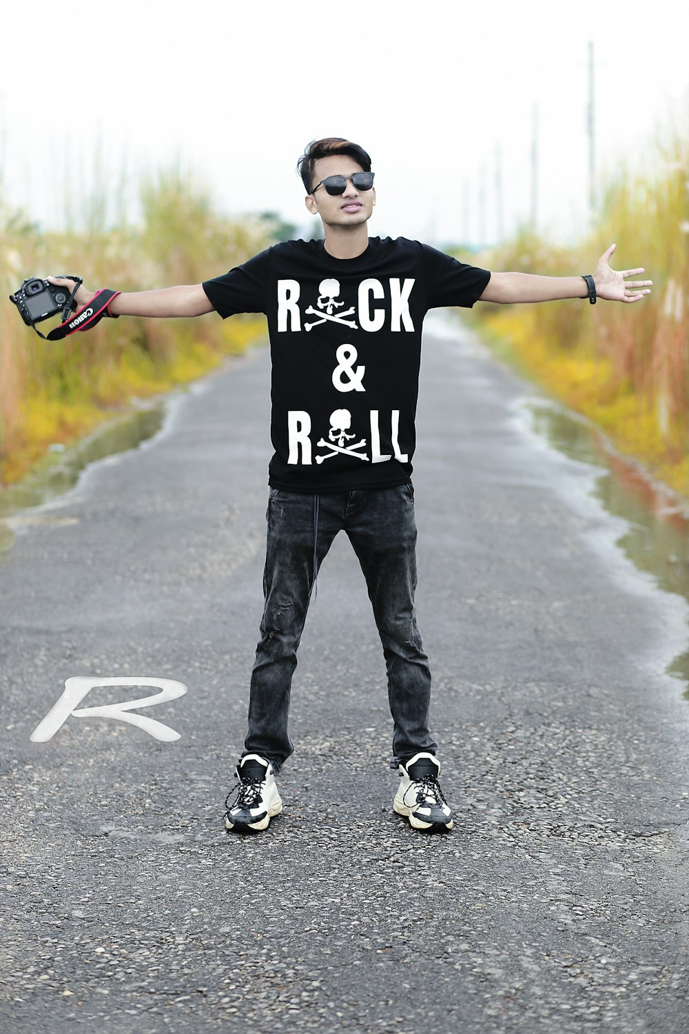 Hombre con camiseta de cuello redondo blanco y negro y jeans de mezclilla negros de pie sobre gris