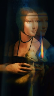 A portrait of a woman wearing a dark dress and a beaded necklace, holding a small animal with light fur. The image includes a soft glow and reflection, creating a mysterious and artistic effect.