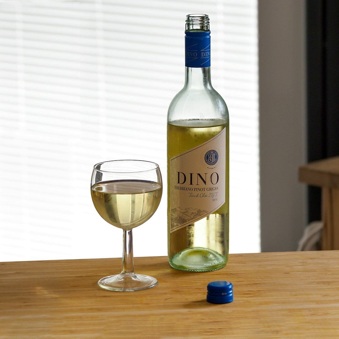 green wine bottle beside clear wine glass on brown wooden table