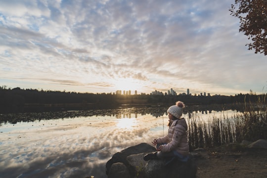 man in white jacket sitting on rock near lake during daytime in Burnaby Canada