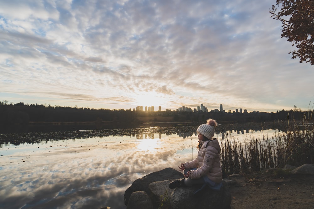 man in white jacket sitting on rock near lake during daytime