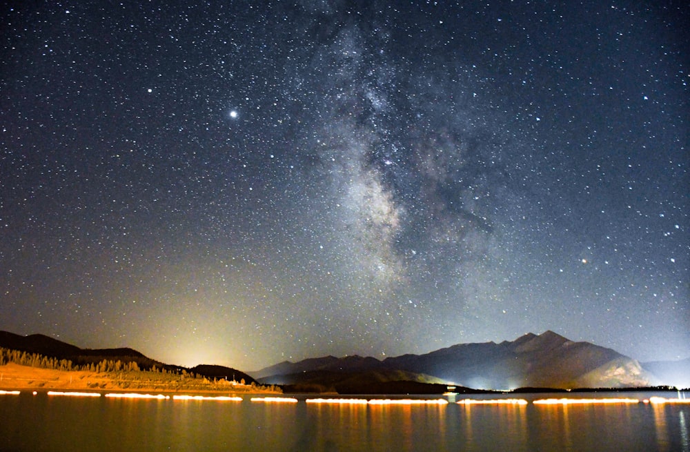 body of water near mountain under starry night