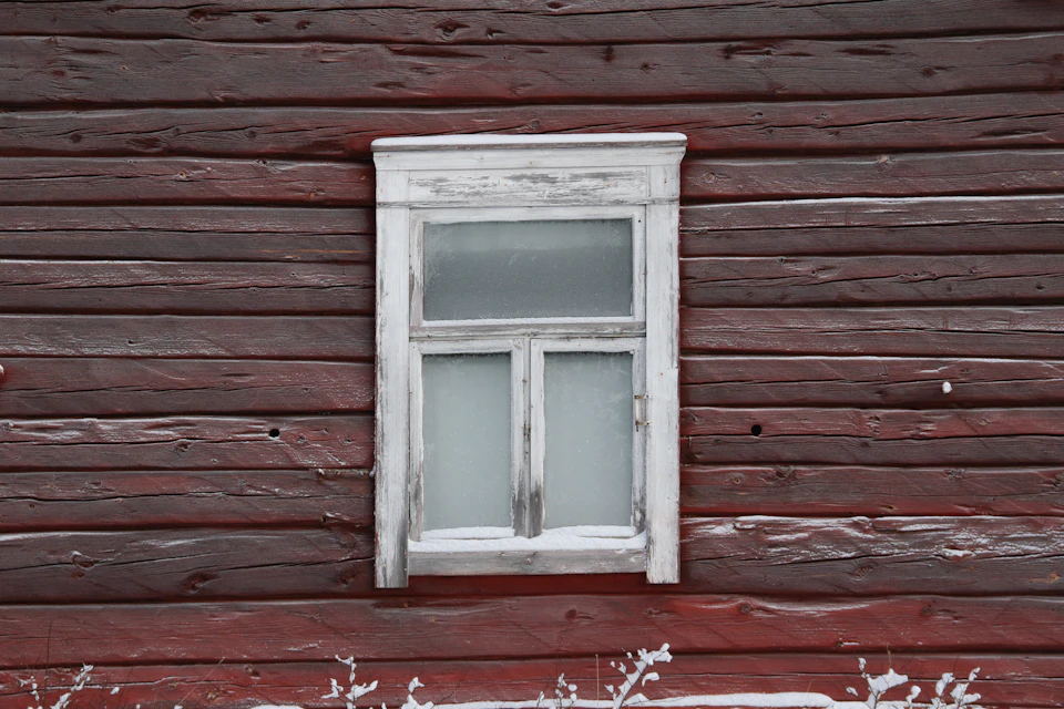 Wooden building with white window on right side, framed by vertical lines and planks