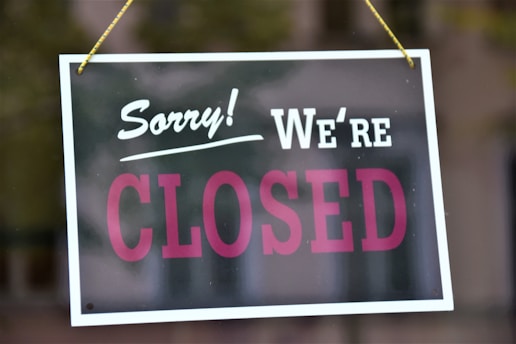 A sign with the words 'Sorry! We're CLOSED' hangs from strings, likely attached to a door or window. The sign features bold white and pink lettering on a dark background with a white border.