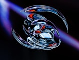 A futuristic and abstract digital artwork featuring intertwined metallic shapes with a glossy finish. The central focus is on smooth, reflective surfaces that merge together, displaying bursts of blue, red, and silver hues. The background is dark, with hints of purple light adding depth and contrast.