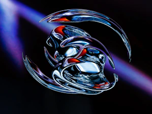 A futuristic and abstract digital artwork featuring intertwined metallic shapes with a glossy finish. The central focus is on smooth, reflective surfaces that merge together, displaying bursts of blue, red, and silver hues. The background is dark, with hints of purple light adding depth and contrast.