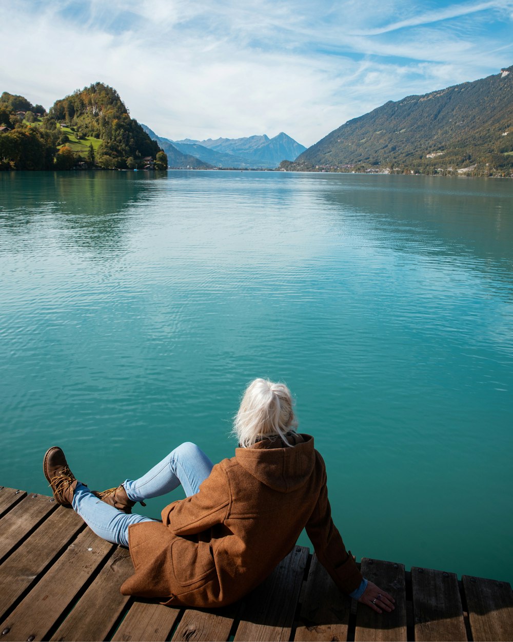 woman in brown jacket sitting on brown wooden dock during daytime