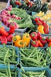A vibrant assortment of fresh vegetables arranged in baskets. There are red and yellow bell peppers, green beans, radishes, leafy greens, and cucumbers.