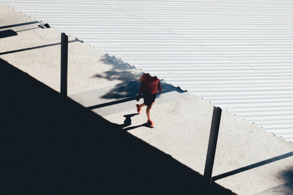 person in red jacket and black pants walking on gray concrete pavement near body of water