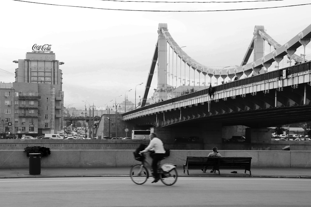 grayscale photo of man riding bicycle on bridge