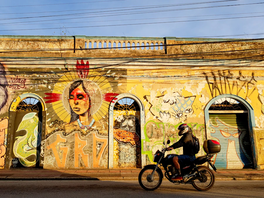Motociclista com baú passando em frente a um muro grafitado e colorido