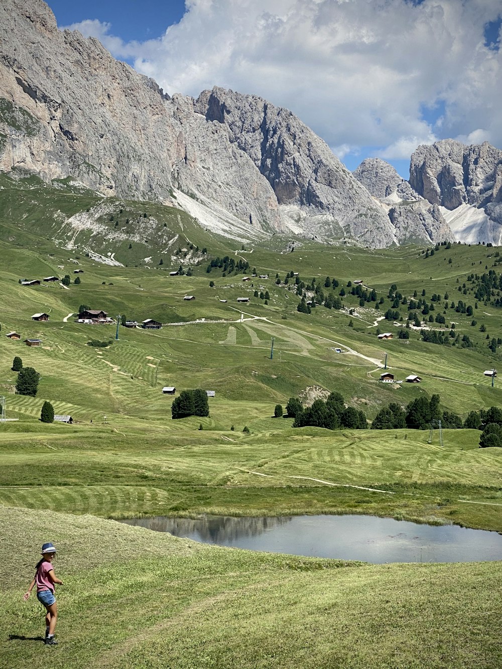 pessoa em jaqueta vermelha andando no campo de grama verde perto do lago e das montanhas durante o dia