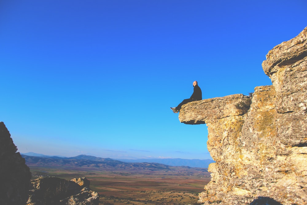 man sitting on rock formation during daytime