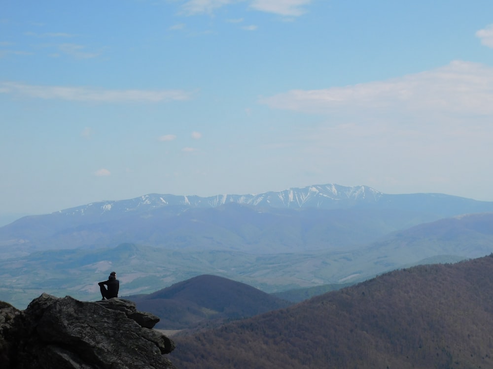 man sitting on rock near mountains during daytime