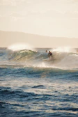 A surfer catching a wave at sunset with volcanic cliffs in the background.
