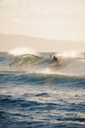 Surfer catching a longboard wave with ocean and mountains in background.