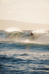 Surfer catching a longboard wave with ocean and mountains in background.