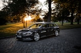 A sleek black luxury car parked in front of the Colosseum at sunset.