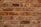 A symmetrical arrangement of unevenly colored red and brown bricks with visible mortar lines. Each brick varies slightly in texture and shade, suggesting handmade or rustic characteristics.