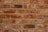 A symmetrical arrangement of unevenly colored red and brown bricks with visible mortar lines. Each brick varies slightly in texture and shade, suggesting handmade or rustic characteristics.