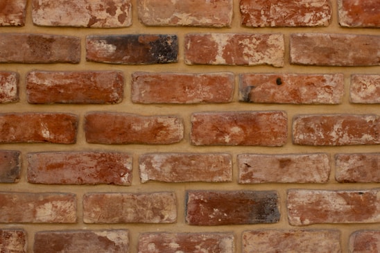 A symmetrical arrangement of unevenly colored red and brown bricks with visible mortar lines. Each brick varies slightly in texture and shade, suggesting handmade or rustic characteristics.