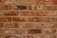 A symmetrical arrangement of unevenly colored red and brown bricks with visible mortar lines. Each brick varies slightly in texture and shade, suggesting handmade or rustic characteristics.