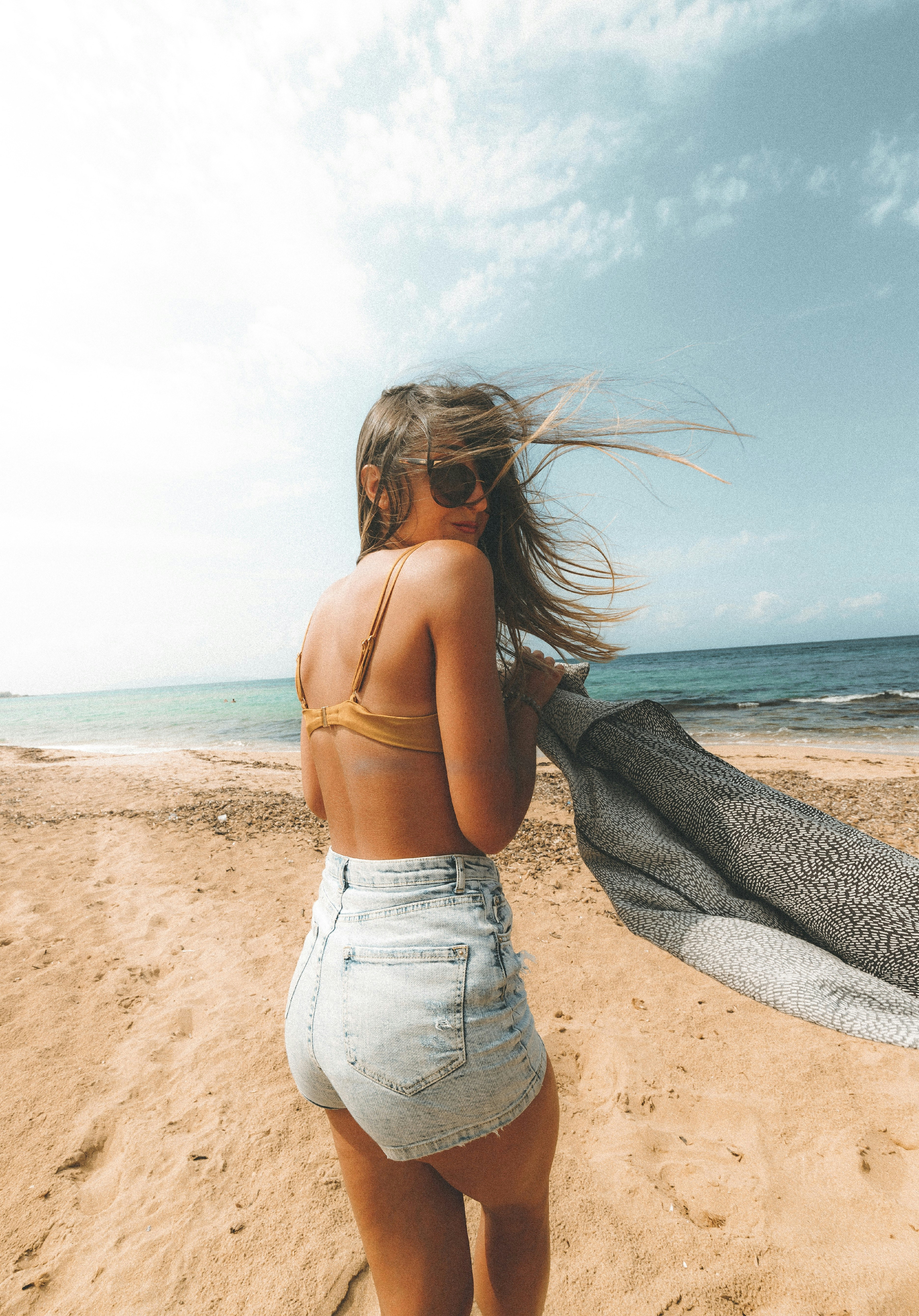 Wanita dengan tank top abu-abu dan jeans denim biru berdiri di pantai di siang hari