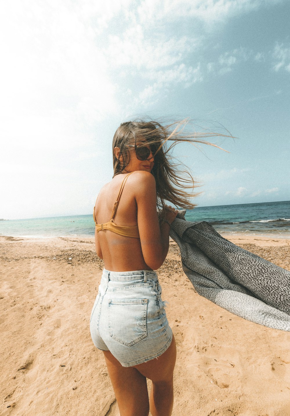woman in gray tank top and blue denim jeans standing on beach during daytime