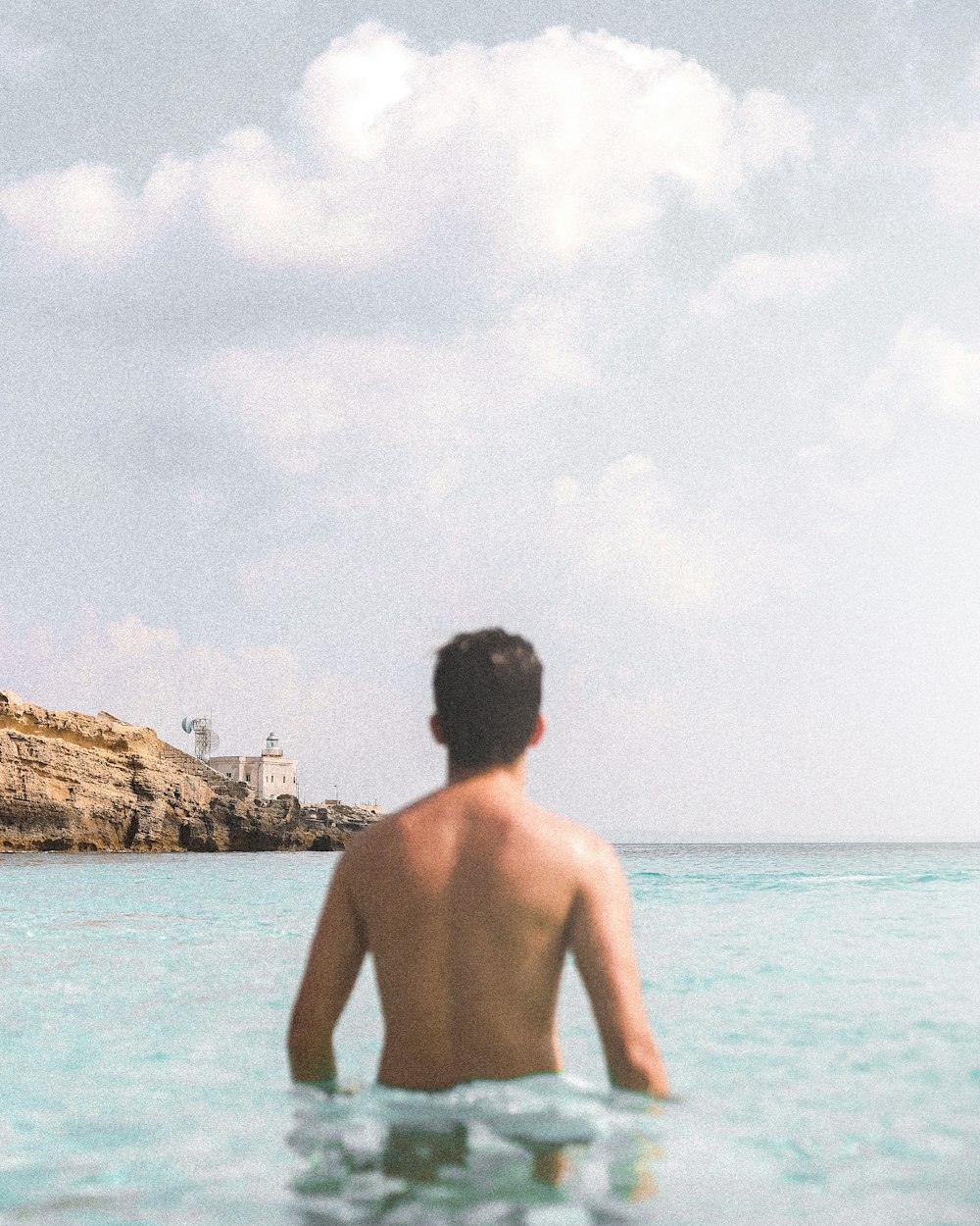 topless man standing on sea shore during daytime