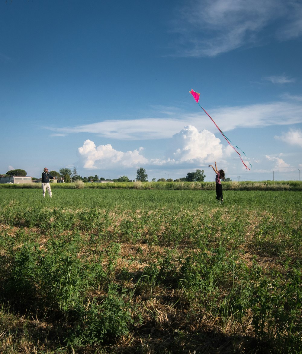 2 men and woman holding red balloons on green grass field during daytime