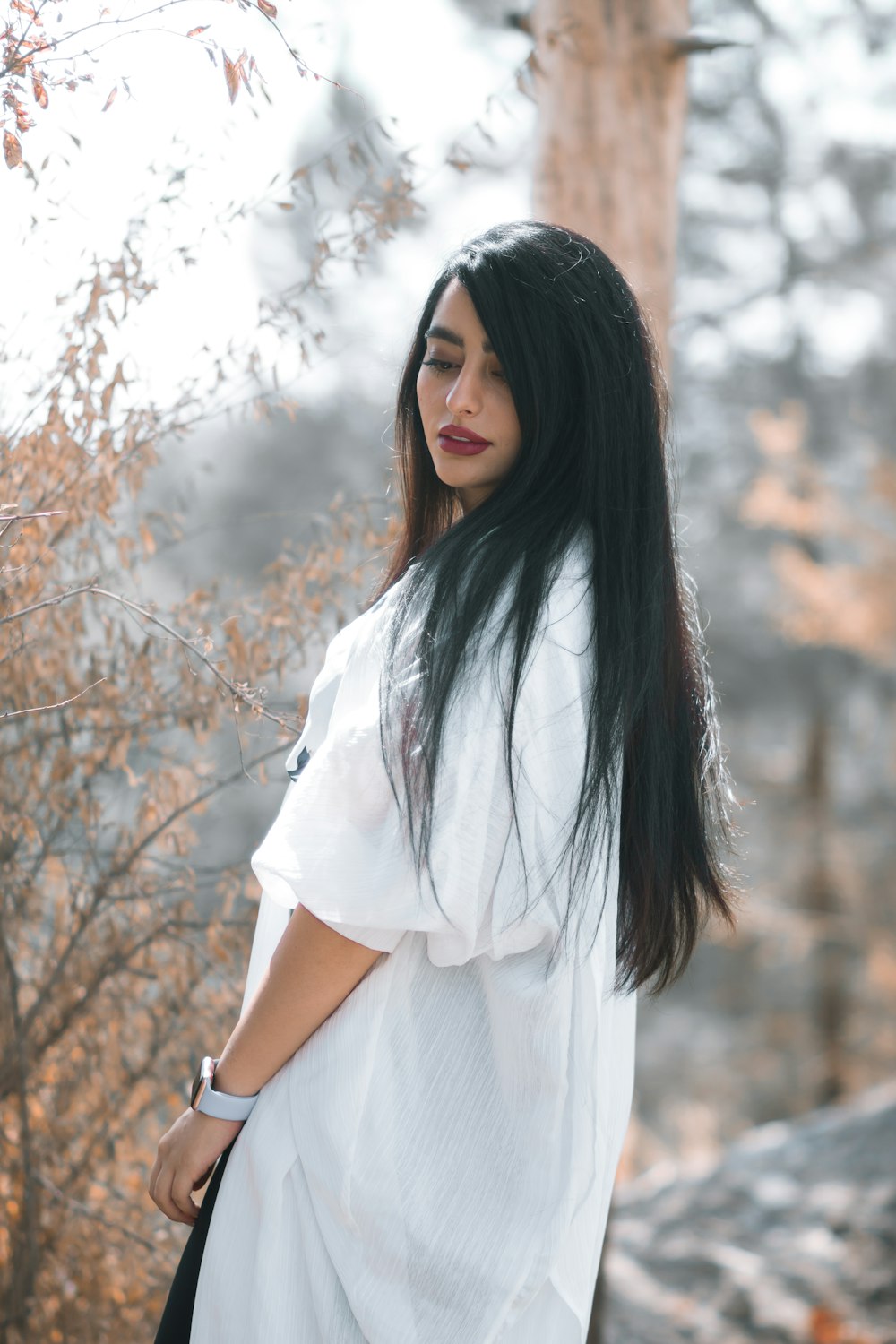 woman in white dress standing near brown trees during daytime