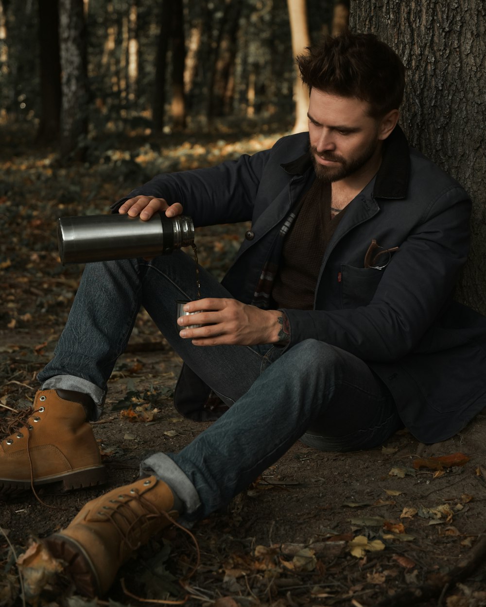 man in black jacket and blue denim jeans sitting on ground while holding silver camera