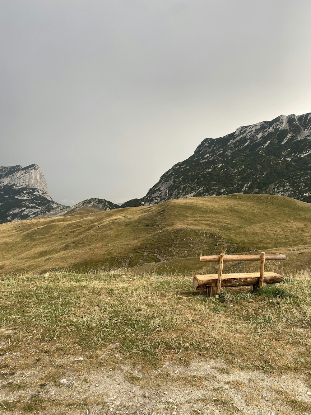 昼間、山の近くの緑の芝生の上の茶色の木製のベンチ