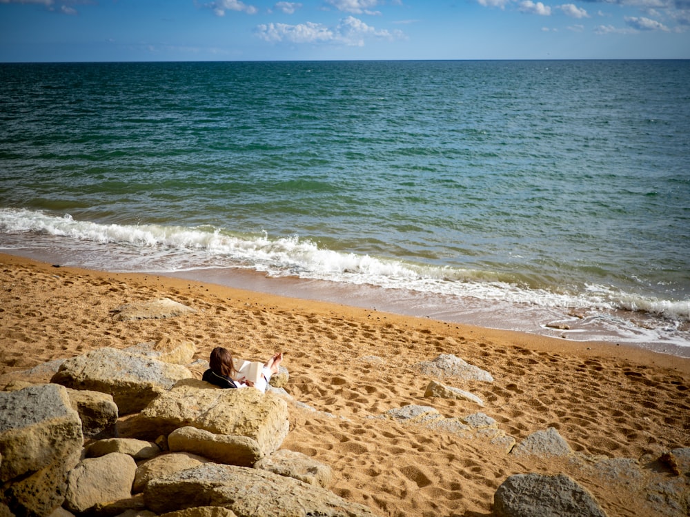 person in white shirt sitting on brown rock near sea during daytime